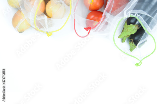 Fresh seasonal tomatoes, eggplants and onions in grocery bags on white background, copy space, flat lay