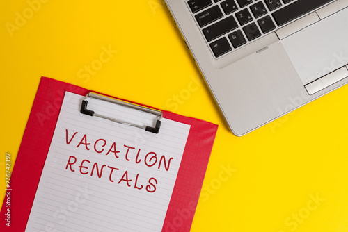 Conceptual hand writing showing Vacation Rentals. Concept meaning Renting out of apartment house condominium for a short stay Part view metallic laptop clipboard paper sheet colored background photo
