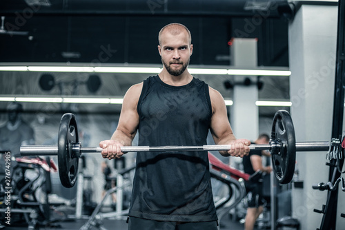 Muscular man working out in gym doing exercises with barbell at biceps, strong male