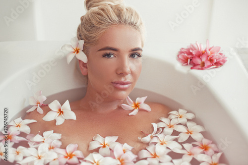 Spa Relax. Blonde enjoying bath with plumeria tropical flowers. Health And Beauty. Closeup Beautiful Sexy Girl Bathing With Petals. Treatment  Aromatherapy Skin Body Care Therapy.
