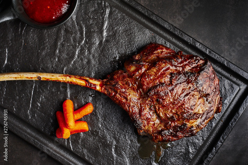 Canvas Print large beef tomahawk steak with sauce at black stone background garnished with french fries