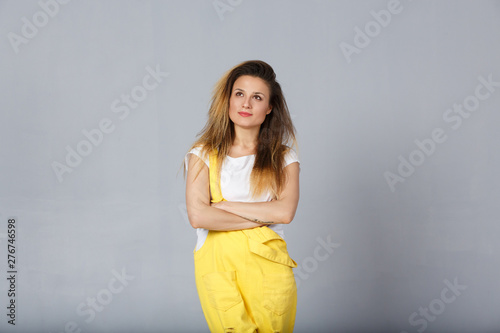 Studio shot of young woman with appealing appearance, has concentrated and dreamful look aside, thinks about future, poses against grey background with blank copy space for your text