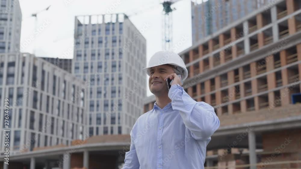 Portrait of a successful young handsome engineer, architect, builder, businessman, wearing a white helmet, in a suit, talking on the phone, skyscraper background and building. 4K Portrait of a successful young handsome engineer, architect, builder, businessman, wearing a white helmet, in a suit, talking on the phone, skyscraper background and building. 4K