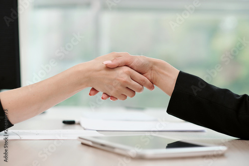 Two beautiful young women in business suits shake hands and smile. Hiring a job. Signing the agreement. Women at work.