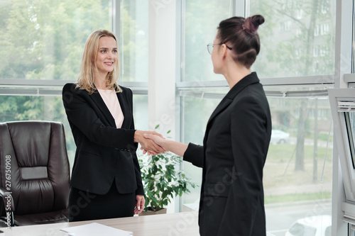 Two beautiful young women in business suits shake hands and smile. Hiring a job. Signing the agreement. Women at work.