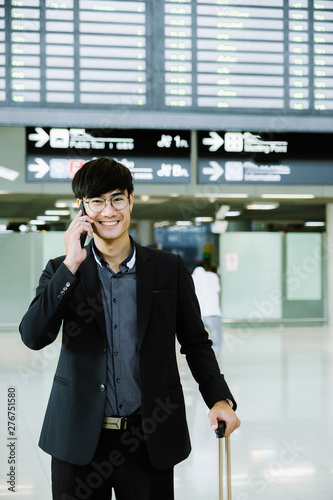 Elegant asian businessman checking email on mobile phone while walking with suitcase inside airport, experienced male employer using cell telephone while waiting for taxi car coming before work travel