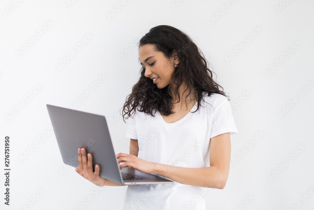 Fototapeta premium Young smiling woman in casual clothes holding laptop and sending email to her best friend