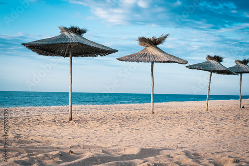 Sandy beach by the sea and wooden sun shelters in the form of umbrellas