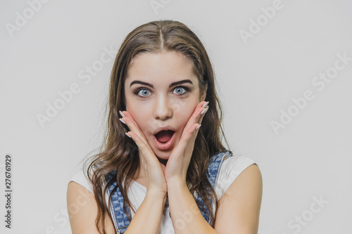 Horizontal portrait of pretty woman with puzled expression, finds solution, wears casual t shirt with denim overalls, isolated over white background. Adorable lovely female student thinks indoor photo