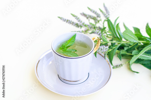 One cup with a saucer of mint tea on a yellow background.