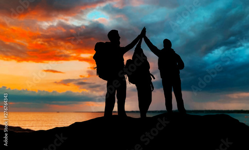travel, tourism and hike concept - group of travelers with backpacks making high five over sunset background