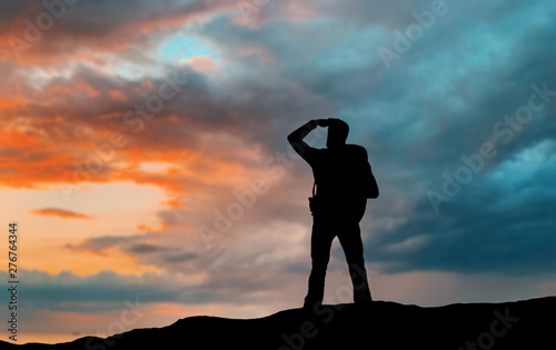 travel, tourism, hike and people concept - traveler with backpack standing on edge of hill and looking far away over sunset background