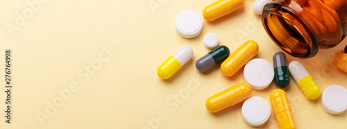 Multicolor tablets and pills capsules from glass bottle on yellow background Health care Close-up Horizontal banner Copy space photo