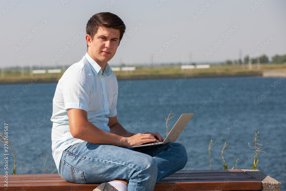 Happy man sitting on bench and using laptop in a park.
