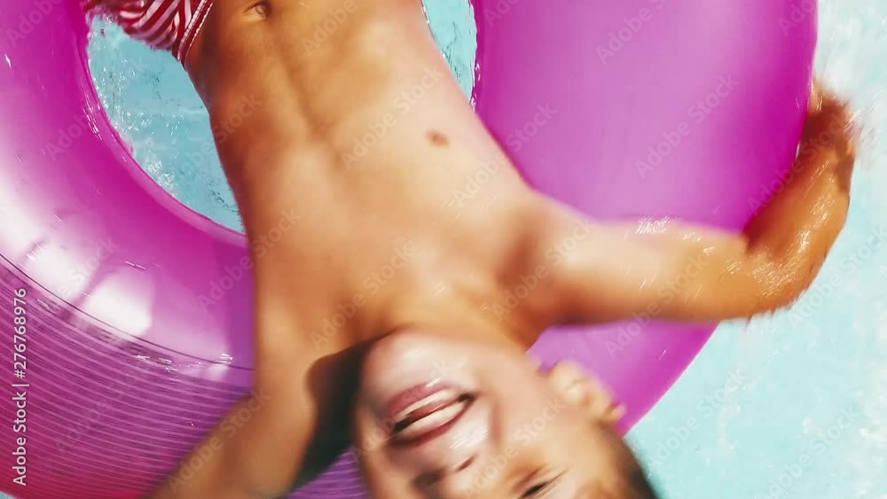 Close up shot of a happy child spinning as his dad spins him around in a pool, with camera angle rising.