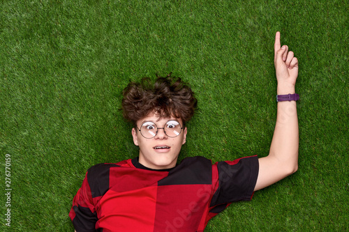 Amazed teen boy pointing up on grass