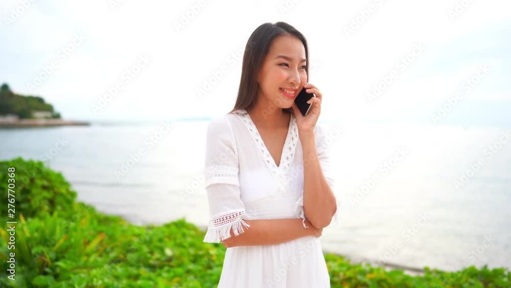 Static portrait medium shot of a sexy beautiful lady wearing a white beach dress while talking on the phone with the ocean blurred in the background Static portrait medium shot of a sexy beautiful lady wearing a white beach dress while talking on the phone with the ocean blurred in the background