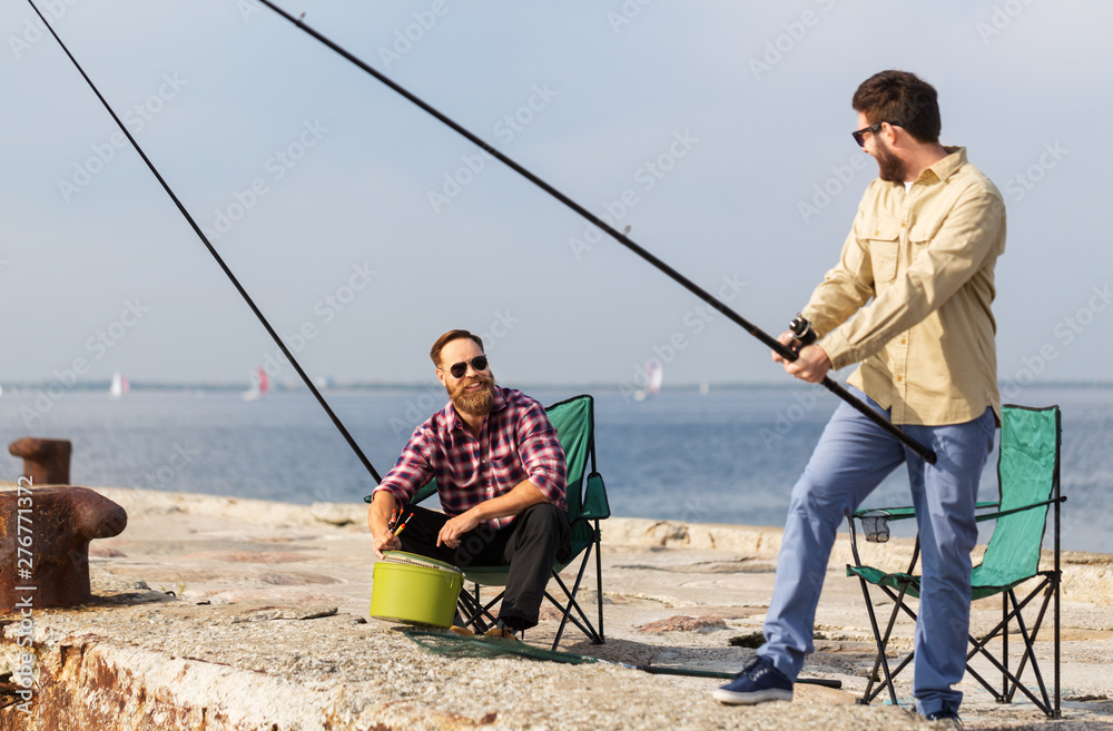 leisure and people concept - male friends with fishing rods on pier at sea leisure and people concept - male friends with fishing rods on pier at sea