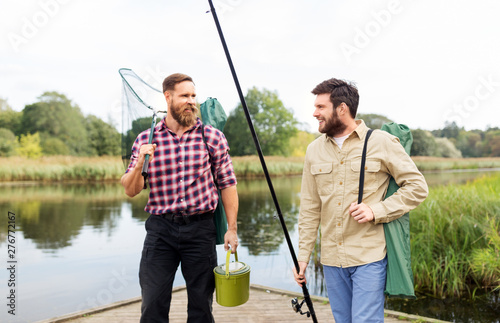 leisure and people concept - male friends with net and fishing rods on lake pier