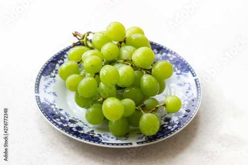 Ripe green grapes in plate on white wooden table, top view. Green grapes in a plate on the table. Green grapes in a red plate on the table.