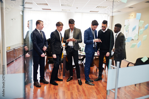 Six multiracial business mans standing at office and use mobile phones. Diverse group of male employees in formal wear with cellphones.