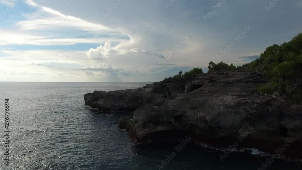 flying up over cliffs and rocky coast of the turquoise Indian Ocean with frothy waves hitting the stones on a cloudy evening. Aerial footage of Blue Lagoon area on Nusa Ceningan island, Bali. flying up over cliffs and rocky coast of the turquoise Indian Ocean with frothy waves hitting the stones on a cloudy evening. Aerial footage of Blue Lagoon area on Nusa Ceningan island, Bali.