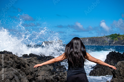 woman arms spread in front of waves crashing on coast rocks