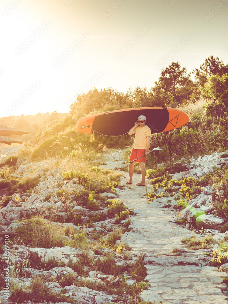 man carrying surfboard and waiting on small path