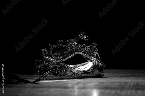 Mask of mystery. A black and white portrait of a venetian mask on a wooden table surrounded by darkness.