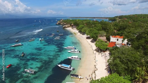 Flying high above Mushroom Beach with yellow sand, lush vegetation, luxury villas, resorts and variety of boats and yachts bobbing on foamy waves of turquoise Ocean. Aerial of Nusa Lambongan, Bali.