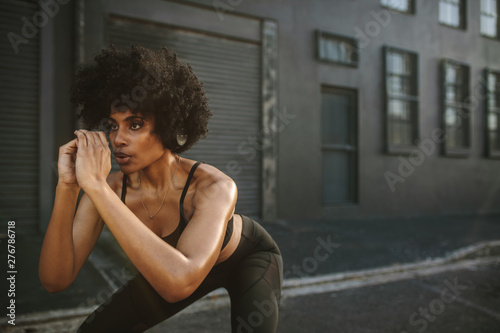 Quadro em tela Young woman exercising squats in city