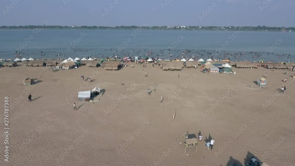 aerial slider shot of crowds of people have gathered to take a swim with wooden bungalows spread over sand beach. aerial slider shot of crowds of people have gathered to take a swim with wooden bungalows spread over sand beach.