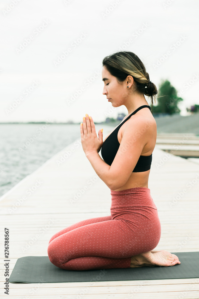 young girl meditating outdoors on the pier by the lake.