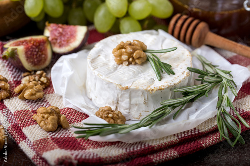 fresh round cheese on linen napkin in white red cage, can of mustard honey, branch of green grapes in bowl of natural wood, slice of figs, rosemary