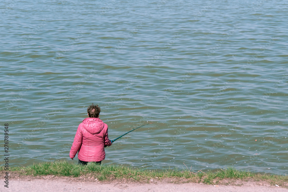 one woman in a pink jacket is fishing on the beach. fishing on the beach at sunny time of the day. old lady fishing alone one woman in a pink jacket is fishing on the beach. fishing on the beach at sunny time of the day. old lady fishing alone