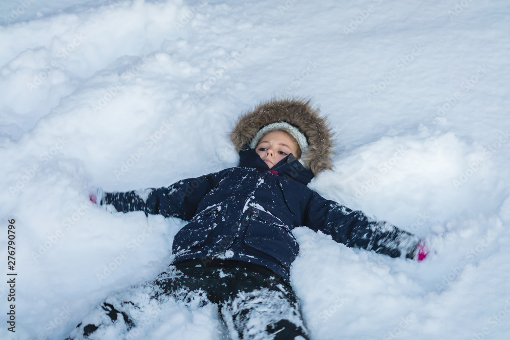 Fototapeta premium Little girl lying in a deep snow