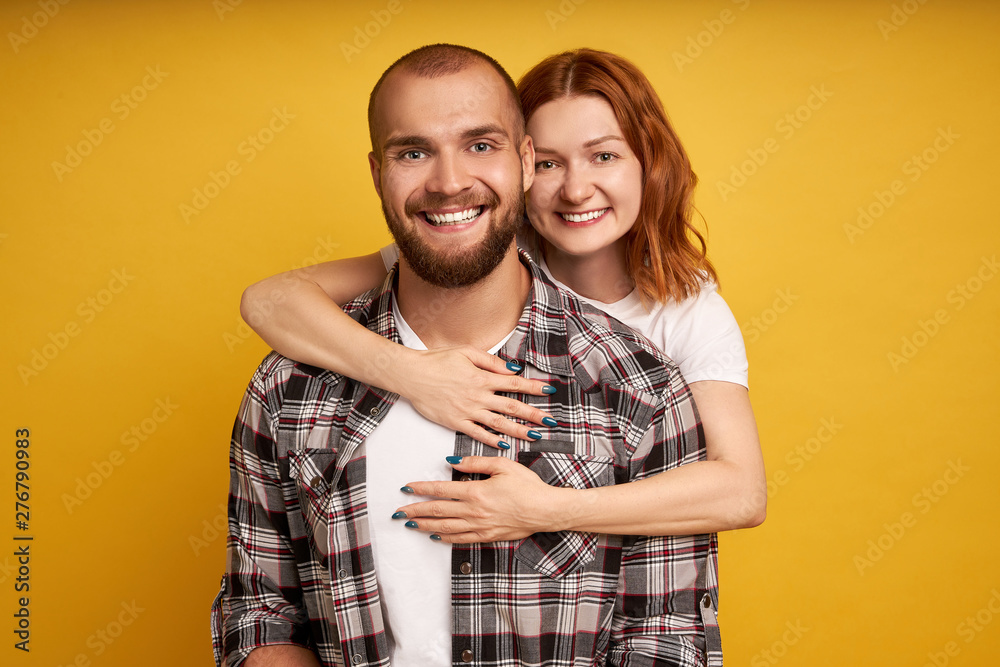 Lovely couple have warm cuddle, pose for family portrait, smile joyfully, have good relationships. Affectionate brother embraces his sister isolated over yellow wall. Couple have date