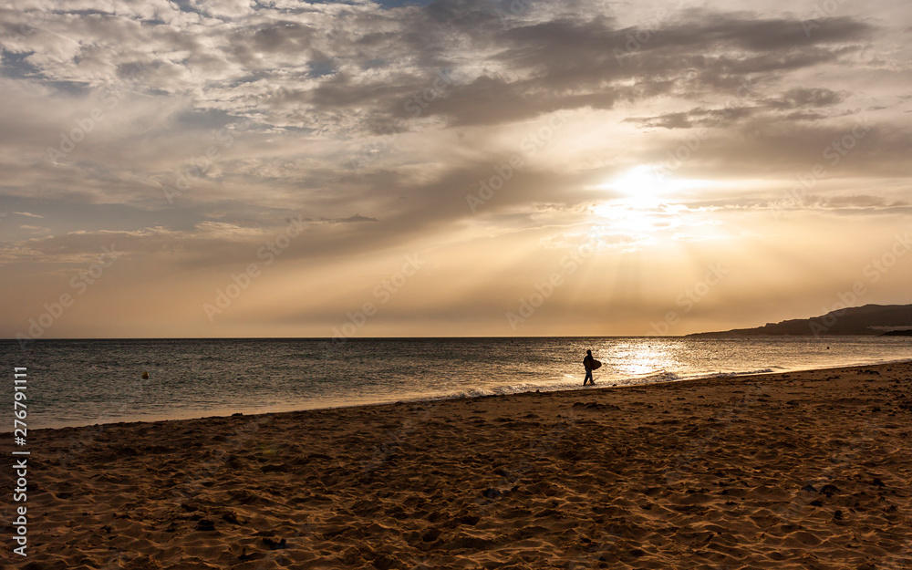 SUNSET WITH LIGHT RAYS AND MAN RIDING BY THE SHORE ON THE COAST OF CADIZ IN SPAIN