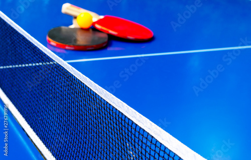 Blue table tennis or ping pong. Close-up ping-pong net. Close up ping pong net and line. Two table tennis or ping pong rackets or paddles and ball on a blue table with net background