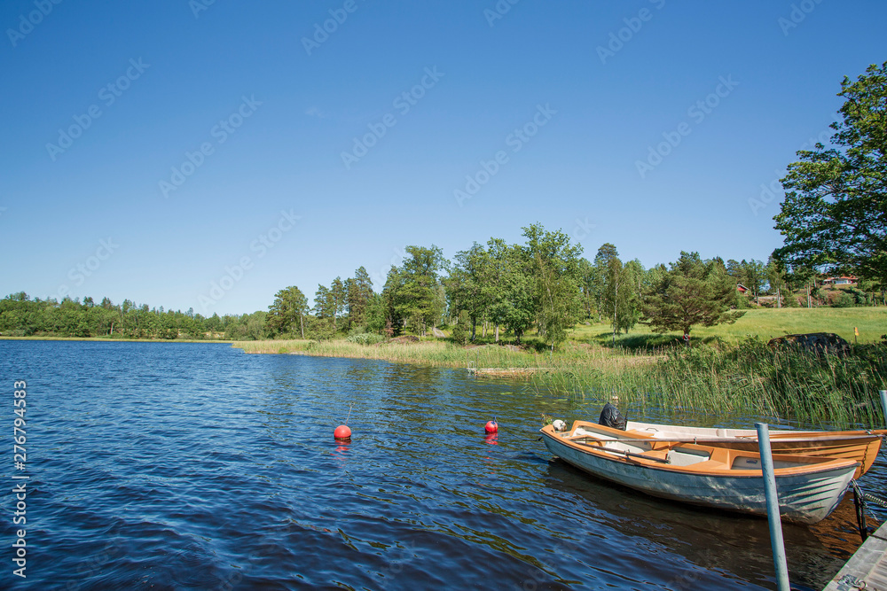 View of lake with two boats parked in shore on blue sky background. Beautiful nature landscape backgrounds.	