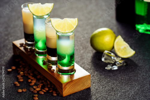 Alcohol Cocktail Drink Shot B52 Green Mexican Set. Layer Beverage with Brown and White Liquor in Small Glass on Wooden Board for Alcoholic Party. Decorated Ice Cubes, Coffee Bean and Lime Wedges