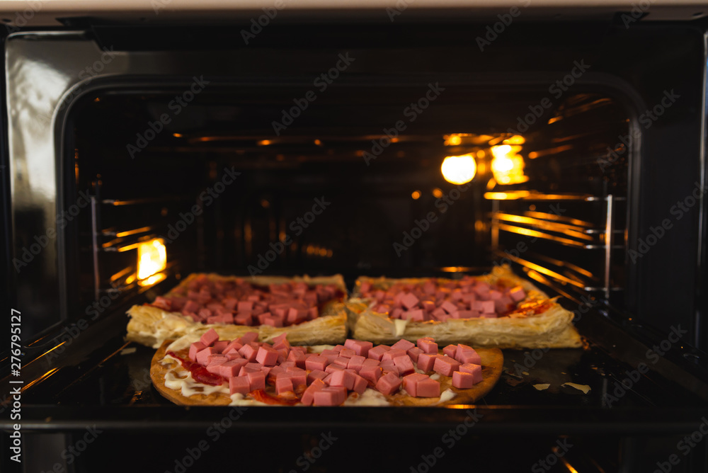 Homemade pizza in the oven close-up, sausage sprinkled with cheese Homemade pizza in the oven close-up, sausage sprinkled with cheese