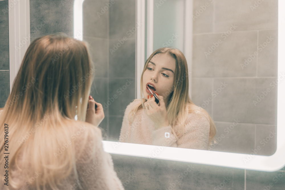 The girl in the bathroom in front of the mirror paints her lips. The girl in the bathroom in front of the mirror paints her lips.