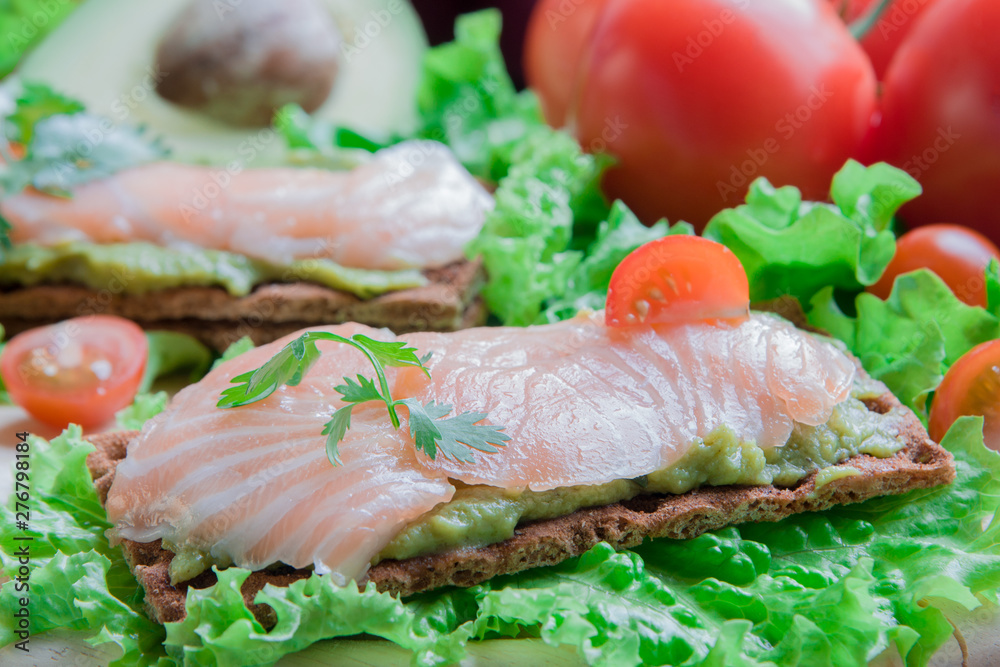 Crispbread with guacamole and salmon on vegetable background