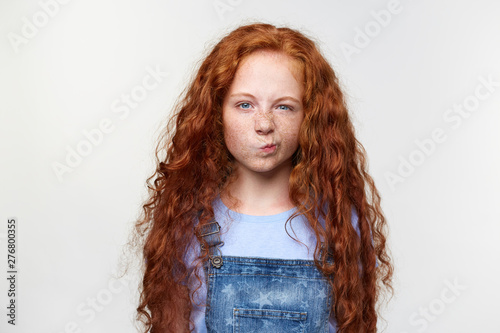 Photo of malcontent nice freckles little girl with ginger hair, parents forbid to watch cartoons, grumpy looks at thecamera, stands over white background. photo