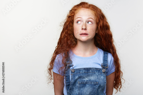 Принти на полотні Portrait of guilty cute freckles little girl with ginger hair, pretends not to do anything wrong, looks away over white background with copy space on the left side