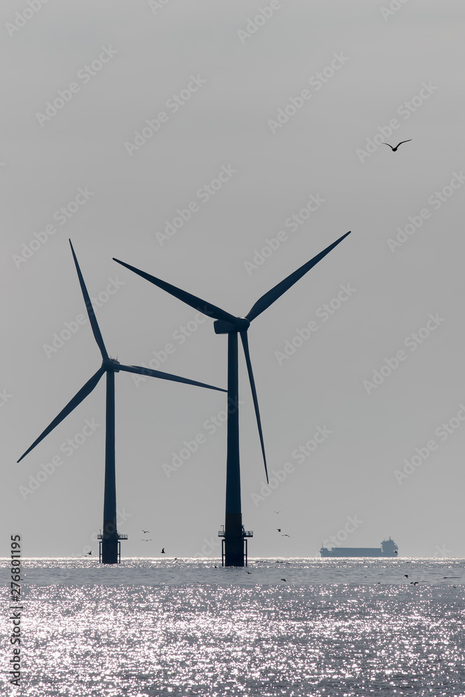 Clean energy production development. Offshore wind power turbine silhouette with supply vessel.