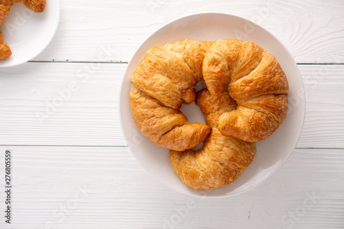 Warm crispy flaky croissant roll on white plate and distressed table.