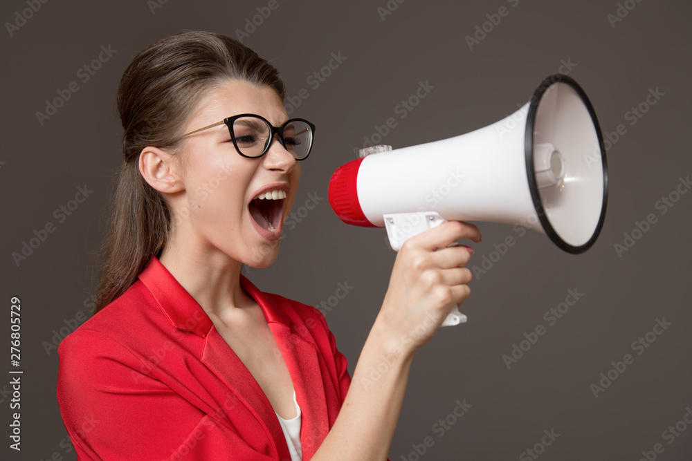 Naklejka premium business woman shouting at a megaphone. Young pretty girl in glasses and a red jacket