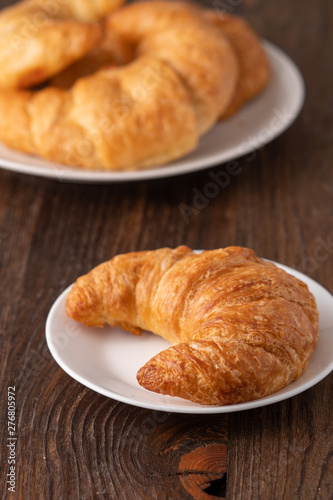 Warm crispy flaky croissant roll on white plate and distressed table.